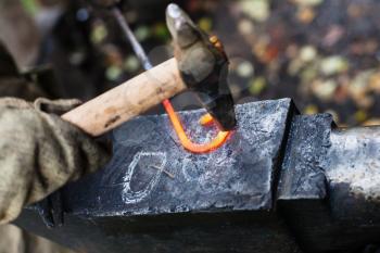 Blacksmith forges iron buckle with hammer on anvil in outdoor rural smithy