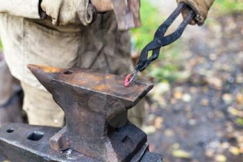 Blacksmith forges a buckle with hammer on anvil in outdoor rural smithy