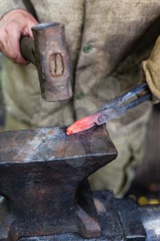 Blacksmith forges tongs with hammer on anvil in outdoor rural smithy
