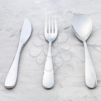 food concept - steel cutlery set from table knife, fork, soup spoon on concrete surface