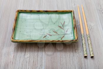 one green square plate and chopsticks on gray brown board