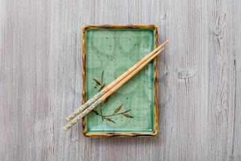 top view of one green square plate with chopsticks on gray brown board