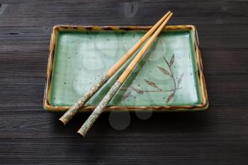 one green square plate with chopsticks on dark brown board