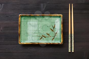 top view of one green square plate and chopsticks on dark brown board