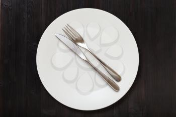 food concept - top view of white plate with parallel knife, spoon on dark brown table