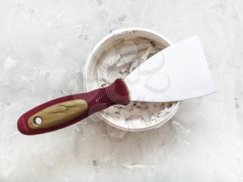 metal spatula with plastic handle on container with putty on the concrete floor