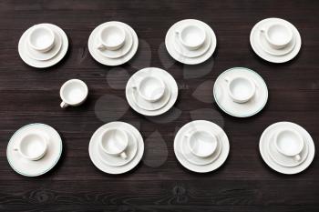 food concept - above view of many white cups and saucers on dark brown board