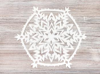 top view of snowflake cut out of paper on light brown wooden board