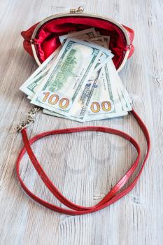 100 dollars banknotes fall out from red leather handbag on wooden table