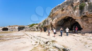 SYRACUSE, ITALY - JULY 3, 2011: tourists near artificial cave with nymphaeum of ancient Greek theater on Temenite Hill in Archaeological Park (Parco Archeologico della Neapolis) of Syracuse, Sicily