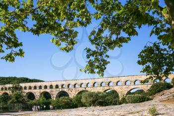 Travel to Provence, France - tourists go to ancient Roman aqueduct Pont du Gard through Gardon River near Vers-Pont-du-Gard town