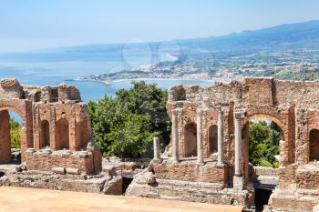 travel to Sicily, Italy - view of ruined walls of Teatro antico di Taormina, ancient Greek Theater (Teatro Greco) in Taormina city and Giardini Naxos town of coast of Ionian Sea