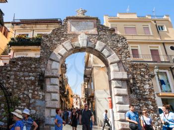 TAORMINA, ITALY - JUNE 29, 2017: tourists walk through old gateway Porta Messina in Taormina city. Taormina is resort town on Ionian Sea in Sicily