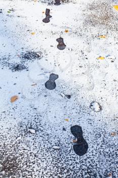 frozen footprints on wet road covered with the first snow in frosty autumn day