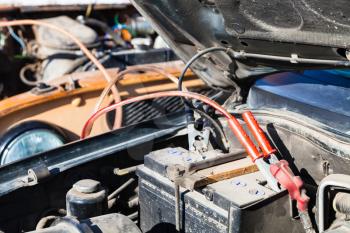 Jump starting a old car battery with another vehicle and jumper leads outdoor