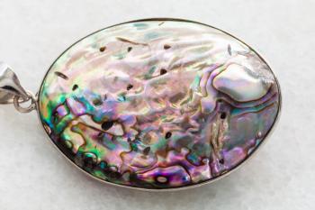 macro shooting of natural mineral rock specimen - pendant from Abalone (haliotis) shell on white marble background