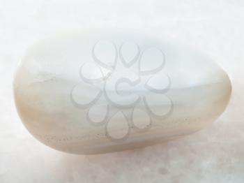 macro shooting of natural mineral rock specimen - polished white Agate gemstone on white marble background