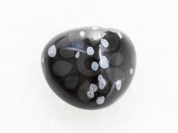 macro shooting of natural mineral rock specimen - tumbled snowflake obsidian gemstone on white marble background