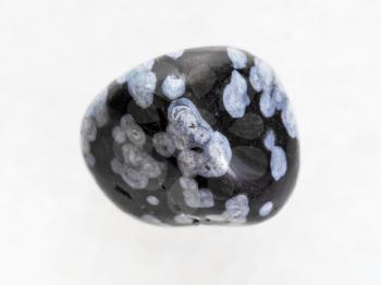 macro shooting of natural mineral rock specimen - polished snowflake obsidian gemstone on white marble background