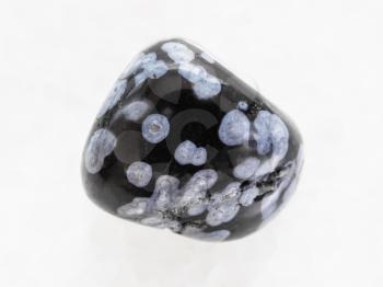 macro shooting of natural mineral rock specimen - tumbled snowflake obsidian gemstone on white marble background