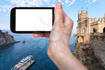 travel concept - tourist photographs pier and Swallow's Nest Castle over Black Sea in Gaspra District on Crimean Southern Coast in september evening on smartphone with cut out screen for advertising