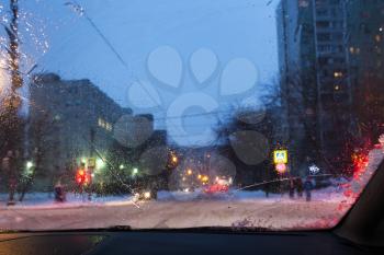 driving in night snowfall in Moscow - unfocused background with view of street in Moscow city in snowy evening through wet windscreen (focus on melting trickle on car glass)