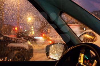 driving in night snowfall in Moscow city in winter evening (focus on car side glass)
