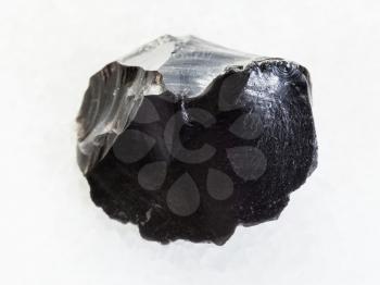 macro shooting of natural mineral rock specimen - raw obsidian (volcanic glass) crystal on white marble background