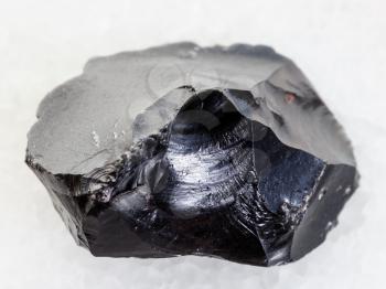 macro shooting of natural mineral rock specimen - rough obsidian (volcanic glass) crystal on white marble background