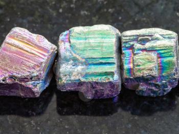 macro shooting of natural mineral rock specimen - beads from rainbow pyrite gemstone on dark granite background