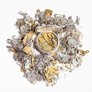 watchmaker workshop - top view of open silver pocket watch on heap of old clock spare parts on white background