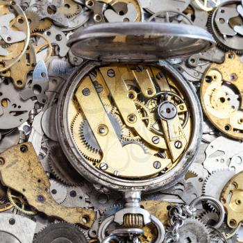 watchmaker workshop - open vintage silver pocket watch with brass clockwork on pile of clock spare parts