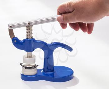 watchmaker workshop - hand holds handle of manual press for closing back cover and crystal glass of wristwatch on white table