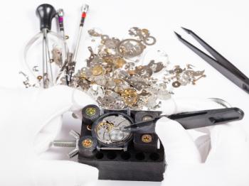 watchmaker workshop - repair of mechanic wristwatch with spare parts by tweezers on white background