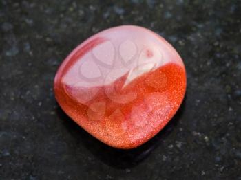 macro shooting of mineral rock specimen - tumbled red goldstone gemstone on dark granite background