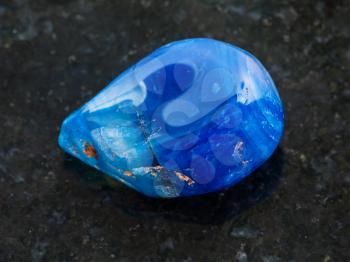 macro shooting of natural mineral rock specimen - tumbled blue toned agate gemstone on dark granite background