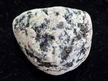 macro shooting of natural mineral rock specimen - pebble of Diorite stone on dark granite background