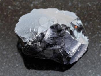 macro shooting of natural mineral rock specimen - rough obsidian (volcanic glass) crystal on dark granite background