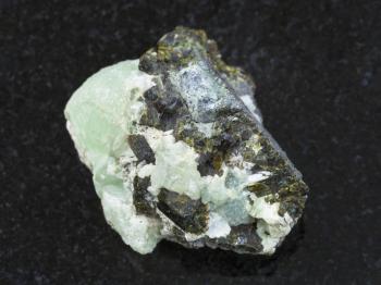 macro shooting of natural mineral stone specimen - Epidote crystals on prehnite gemstone on dark granite background