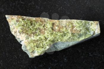 macro shooting of natural mineral rock specimen - rough crystal of green Vesuvianite gemstone on dark granite background from Bazhenovskoe mine, Sverdlovsk region, Ural Montains, Russia