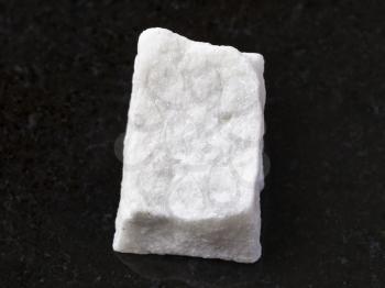 macro shooting of natural mineral rock specimen - piece of rough white marble stone on dark granite background