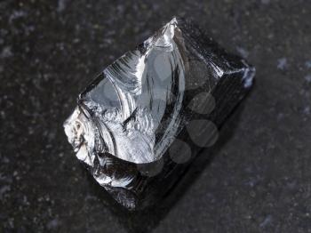 macro shooting of natural mineral rock specimen - piece of raw Obsidian (volcanic glass) stone on dark granite background