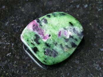 macro shooting of natural mineral rock specimen - tumbled zoisite (anyolite) gemstone on dark granite background
