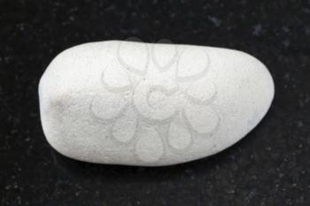 macro shooting of natural mineral rock specimen - tumbled white Limestone gemstone on dark granite background