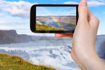 travel concept - tourist photographs rainbow over Gullfoss waterfall on Olfusa river canyon in Iceland in september on smartphone