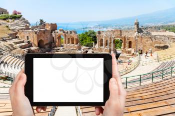 travel concept - tourist photographs ancient Greek Theater (Teatro Greco, Teatro antico di Taormina) in Taormina city in Sicily Italy in summer on tablet with cut out screen for advertising logo
