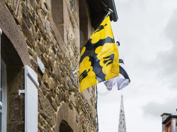 travel to France - yellow St Ivo's (Saint-Yves) flag of Tregor province and white Breton flags on wall of urban house in Treguier town in the Cotes-d'Armor department of Brittany in summer rainy day