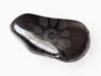macro shooting of natural mineral rock specimen - tumbled black obsidian gemstone on white marble background from Mexico