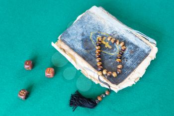 old church book, worry beads and three wooden dices on green baize table