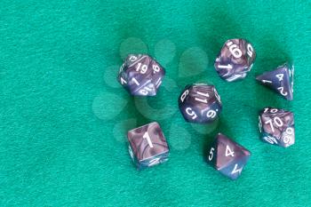 gray polyhedral dices for Dungeons and Dragons board game playing on green baize table with copyspace
